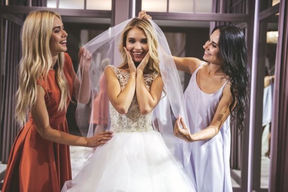 stock-photo-beautiful-bride-is-trying-on-an-elegant-wedding-dress-in-modern-wedding-salon-her-friends-are-2397812483.jpg
